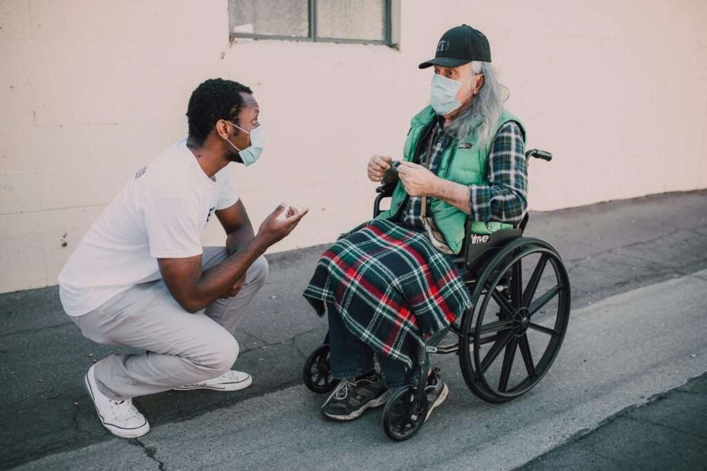 Two people engage thoughtfully outdoors, exemplifying kindness amidst pandemic conditions, one in a wheelchair.
